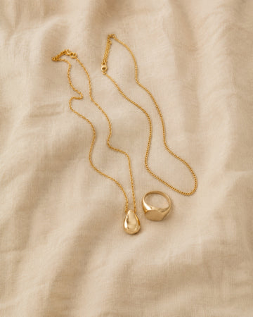 Fine gold chains, pendant and signet ring on softly rumpled bone linen