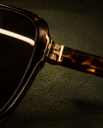 Macro view of dark tortoiseshell sunglasses on deep olive suede