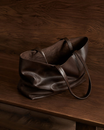 Soft slouched chocolate leather tote on a dark walnut bench