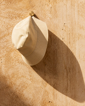 Bone canvas bucket hat hanging on warm travertine with a long shadow