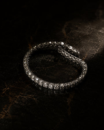 Crystal tennis bracelet under a dramatic spotlight on near-black polished stone
