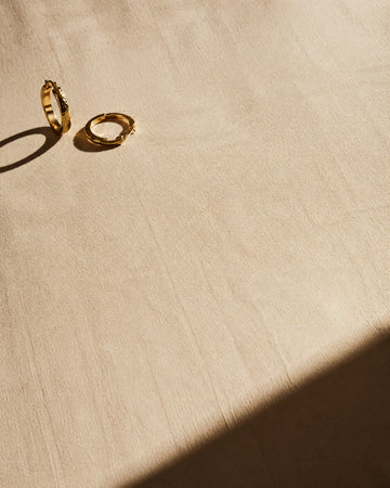 Pair of textured gold hoop earrings casting long shadows on bone linen