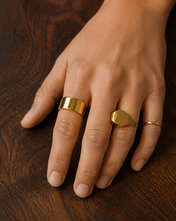 Three gold rings worn on a relaxed hand resting on dark walnut