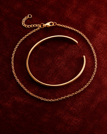 Fine gold chain bracelet and polished cuff on rich oxblood velvet