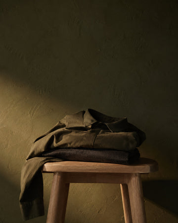 Folded charcoal knit and olive overshirt on a pale oak stool