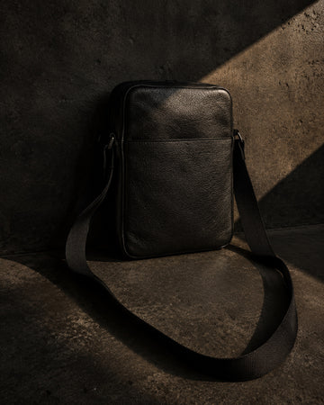 Black leather crossbody bag with loose strap on raw charcoal concrete